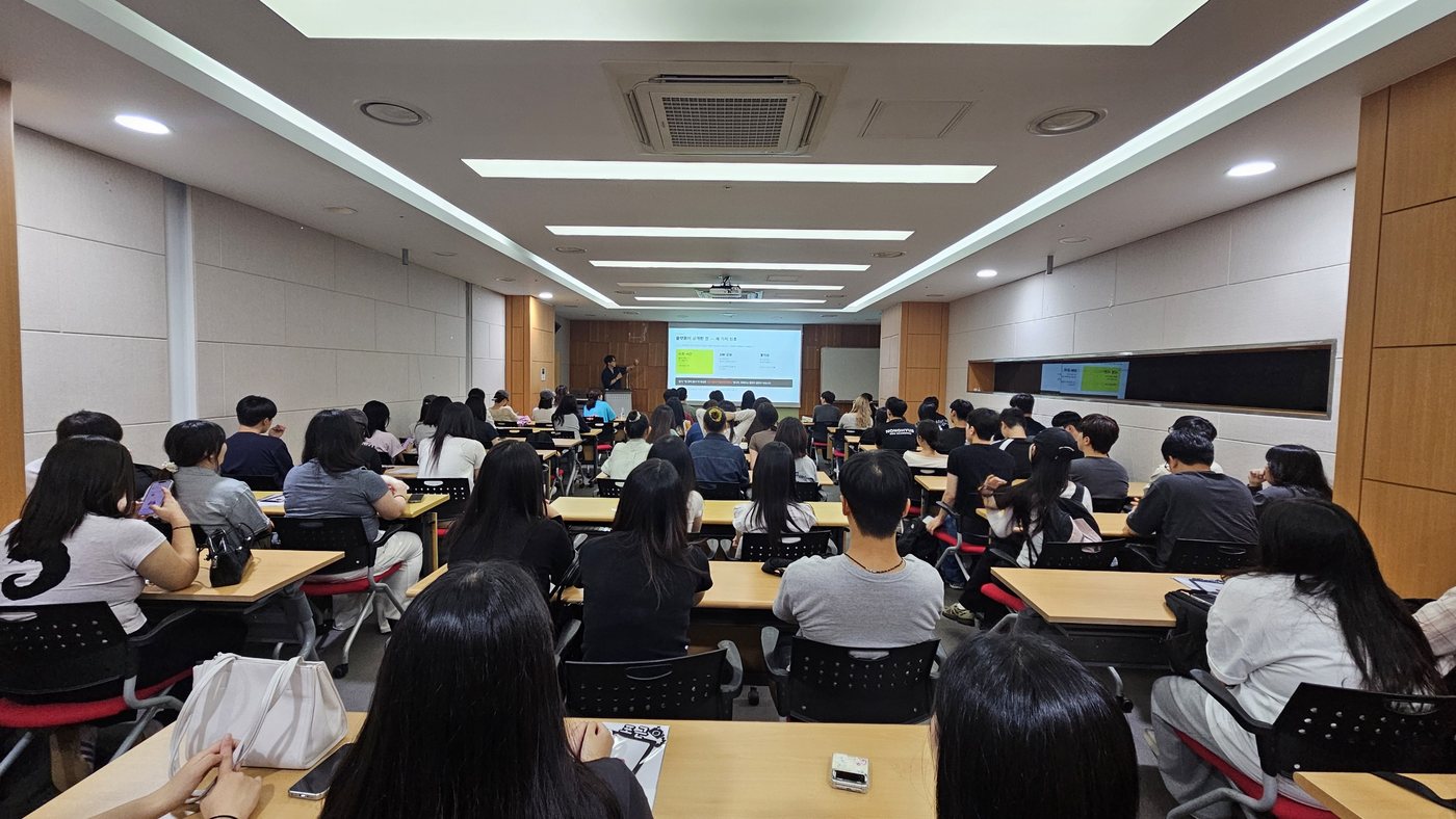 강의실 뒤쪽 넓은 각도에서 촬영한 전경. 좌석이 가득 찬 회의실