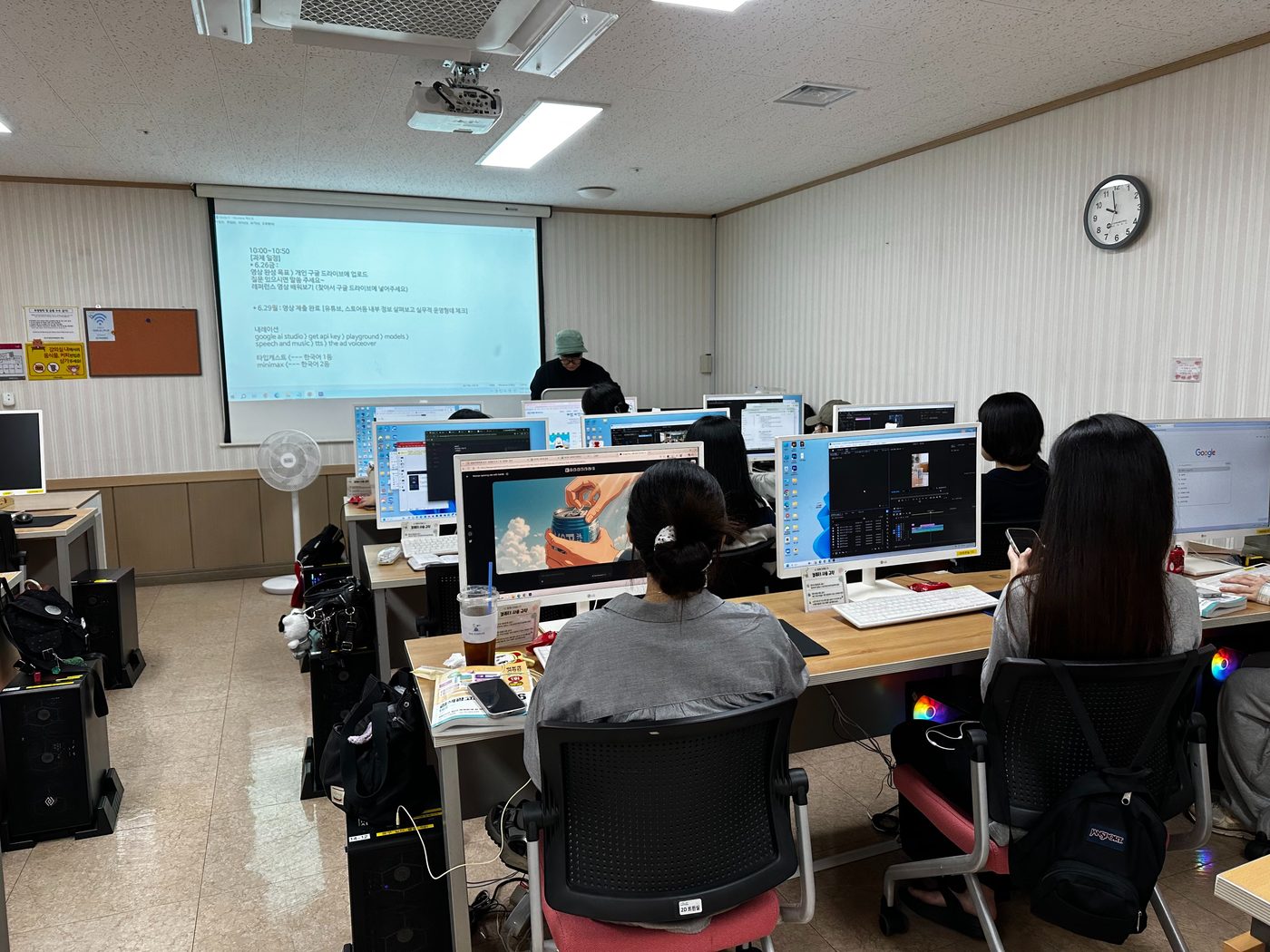 스크린에 포트폴리오 영상 제출 일정과 AI 내레이션 도구 경로가 정리된 화면이 떠 있고 수강생들이 각자 자리에서 편집 작업을 하고 있다