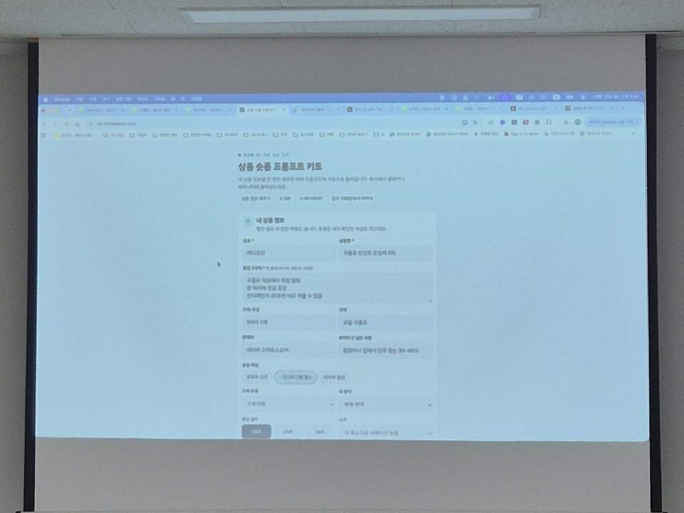 빔프로젝터 화면에 띄운 상품 숏폼 프롬프트 키트 입력 화면. 상호 바다곳간, 상품명 구룡포 반건조 오징어 5미, 특징 세 가지와 올릴 채널, 영상 길이 선택 칸이 보인다