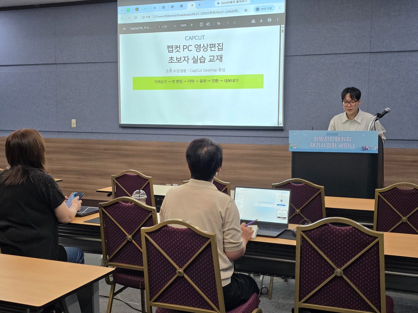 캡컷 PC 영상편집 초보자 실습 교재 표지를 화면에 띄우고 연단에서 설명하는 김재석 강사