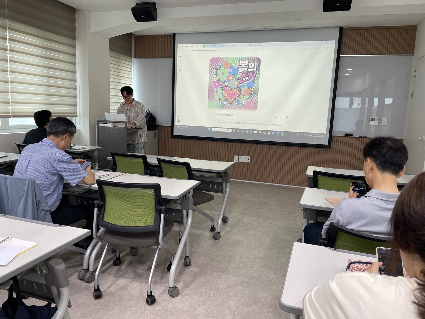 배산평생학습관 강의실에서 AI로 만든 브랜딩용 이미지를 화면에 띄우고 설명하는 장면. 수강생들이 각자 스마트폰으로 따라 하고 있다
